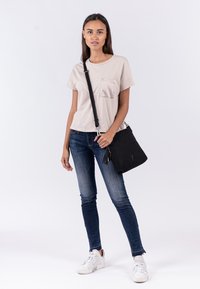 T-shirt beige a maniche corte con taschino, jeans skinny blu scuro e borsa a tracolla nera con nappina. Sneakers bianche completano l'outfit.