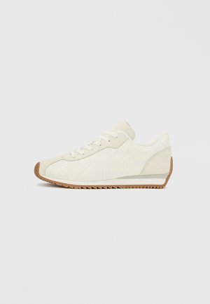 Sneaker bianca con superficie testurizzata e suola in gomma colorata, caratterizzata da profilo basso, punta rotonda e chiusura con lacci. Dettagli laterali comprendono un motivo decorativo.