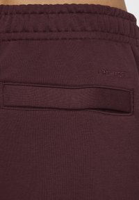 Bordeaux joggers tillverkade av mjukt tyg med midjeband i elastiskt material, utrustade med en liten bakficka och präglad "Dri-FIT"-logotyp.