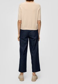 Top beige lavorato a maglia con maniche corte, abbinato a pantaloni a gamba larga blu scuro e scarpe chunky beige chiaro. Design semplice e minimalista.