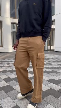 Beige cargo pants with multiple pockets and a loose fit, paired with a black sweatshirt. The footwear features a two-tone design.