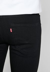 Jeans em denim preto com um corte justo, costura discreta e um design distinto do bolso traseiro com uma etiqueta vermelha da Levi's.