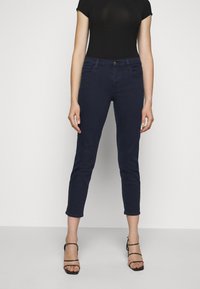 Mörkblå slim fit jeans i denim, med knappstängning och fem fickor. Matchas med en svart figursydd topp och remsandaler.