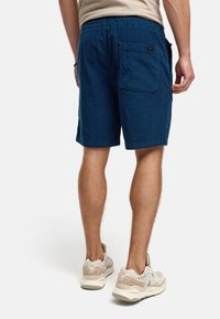 Shorts en velours côtelé bleu avec une taille élastique, dotés d'une poche arrière et d'une coupe au-dessus du genou, associés à des sneakers clairs.