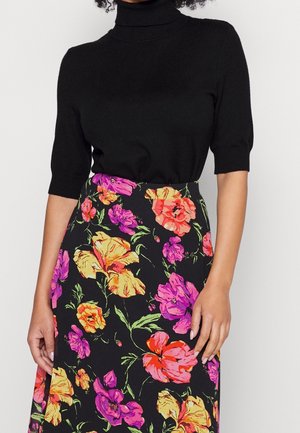 Mannequin portant un haut noir à col roulé et à manches courtes, ainsi qu’une jupe noire à imprimé floral vif rose, orange et jaune.
