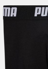 Črne športne legice iz tkanine z širokim elastičnim pasom in belim logotipom "PUMA". Gladka tekstura in oprijet kroj.