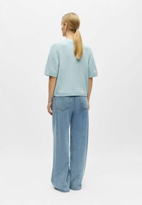 Pull en tricot bleu clair à manches courtes associé à un jean taille haute à jambes larges et délavé clair. Motifs simples et texturés visibles.