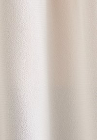 Tissu beige clair avec un motif texturé subtil. Le tissage crée une apparence douce et lisse, adaptée à l'ameublement ou aux rideaux.