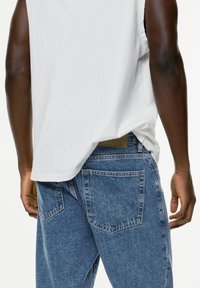 Fitted white sleeveless shirt paired with high-waisted, blue denim jeans featuring a faded texture and two back pockets.