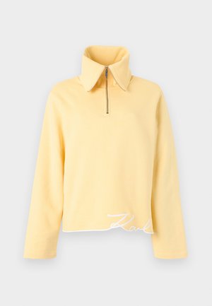 Κίτρινο πουλόβερ με φερμουάρ, φαρδιά γιακά, μακριά μανίκια και κοντό τελείωμα. Διαθέτει κεντητό κείμενο "Karl" σε λευκό χρώμα στο κάτω μέρος.