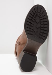 Botte basse en cuir marron avec un extérieur texturé, une fermeture éclair latérale et une semelle en caoutchouc noire robuste avec un motif à relief.
