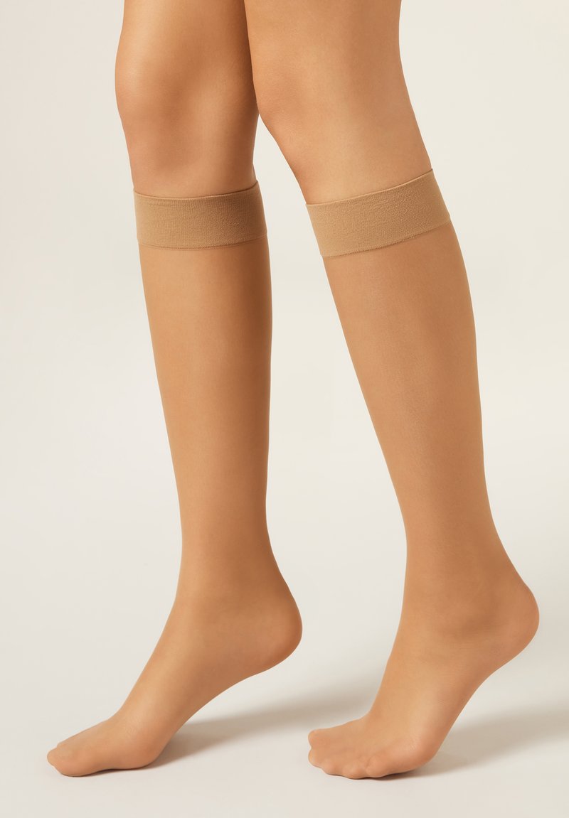 Kniestrümpfe in Nude-Farbe mit glatter Textur und elastischen Bündchen oben. Durchsichtige Optik betont den Hautton.