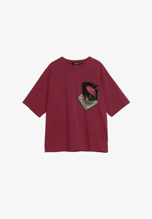 Red oversized t-shirt made of cotton, featuring a black pocket with bird illustrations and a patterned accent at the bottom.