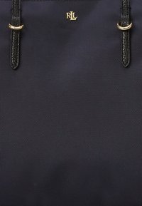 Tyrkysová nylonová taška s černými koženými akcenty, s zlatým logem a dvěma odolnými uchy. Texturovaný povrch přidává jemný detail.