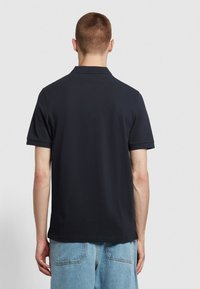 Koszulka polo z krótkim rękawem w ciemnonavy materiału, z kołnierzykiem i żebrowanymi mankietami. Widok z tyłu ukazuje czyste linie i klasyczny krój.