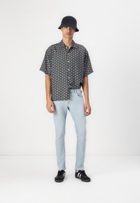 Lyhythihainen musta kuvioitu paita, vaaleansiniset slim-fit farkut, mustat tennarit valkoisilla raidoilla ja tumma hattu.
