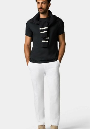 Zwart T-shirt met korte mouwen, witte broek en een marineblauwe trui over de schouders gedrapeerd. De trui heeft een ribbelstructuur en witte strepen.