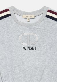 Šedá mikina s rebrovaným okrúhlym výstrihom, s vyšívaným logom a nápisom "TWINSET" z čiernych kamienkov. Prúžkové akcenty v marhuľovej a námorníckej modrej.