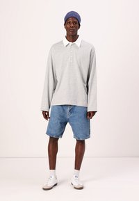 Grå langermet polo-skjorte med hvit krage og knapper, sammen med blå denimshorts. Hvite sneakers og en blå strikket lue fullfører antrekket.