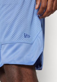 Pantaloni corti in rete blu chiaro con un pannello inferiore liscio. Presentano un piccolo logo ricamato in blu abbinato vicino all'orlo.