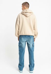 Beżowy oversize'owy hoodie z kapturem na sznurku, zestawiony z jasnoniebieskimi spodniami cargo z bocznymi kieszeniami i luźnym krojem.