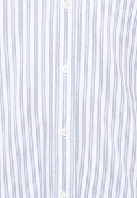 Chemise blanche à fines rayures verticales bleues et boutons blancs au centre.