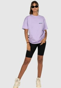 Hellblau oversized T-Shirt mit einem kleinen schwarzen Logo, kombiniert mit schwarzen Radshorts und weißen High-Top-Sneakern.