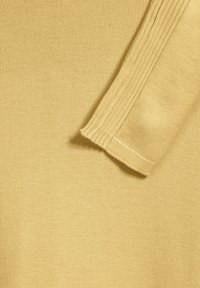 Žlutá pletená látka svetry s podrobnými ribovými manžetami, která se vyznačuje hladkou strukturou a jednotným vzhledem po celém povrchu.