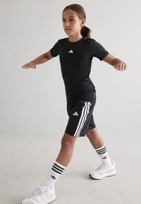 Black athletic t-shirt with white logo, black shorts featuring white stripes, and white footwear with black accents and striped socks.