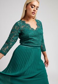 Teal klänning med spetslivstycke som har v-ringning och trekvartsärmar. Plisserad kjol ger textur. Slät satinkant i midjan.