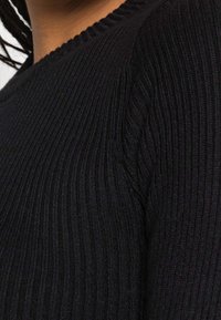 Pull en tricot noir à côtes avec un col rond et un tissu texturé, avec une vue rapprochée mettant en valeur le motif et la forme.