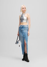 Srebrni crop top s visokim ovratnikom, uparen s uskom traper suknjom koja ima bočni prorez. Model nosi crne platforme i srebrnu torbu.