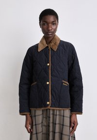 Casaco acolchoado azul-marinho com colarinho em veludo, botões dourados e acabamentos em cor de areia. Apresenta dois bolsos com bordado em dourado "Barbour".