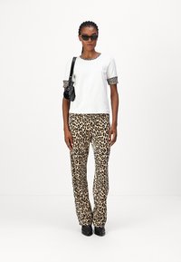 White short-sleeve top with leopard-print cuffs, paired with leopard-print pants, smooth texture, relaxed fit, complemented by black accessories.
