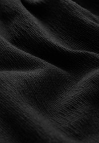 Schwarzer, strukturierten Stoff mit sichtbarem Rippmuster, das eine weiche, zerknitterte Oberfläche und Farbgleichmäßigkeit zeigt. Geeignet für Kleidung oder Polsterung.