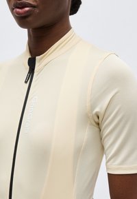 Κοντινό πλάνο ενός ατόμου που φοράει ανοιχτό μπεζ ποδηλατική μπλούζα με μαύρο φερμουάρ στο μπροστινό μέρος και λογότυπο "GripGrab" στο στήθος.