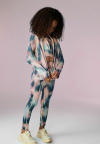 Athletická souprava z měkké elastické látky s modro-růžovo-krémovým tie-dye vzorem, dlouhými rukávy a odpovídajícími přiléhavými legínami se světlými akcenty.
