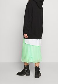 Felpa nera oversize, indossata sopra una gonna plissè verde menta. Stivaletti neri alla caviglia con fibbie e suola robusta.