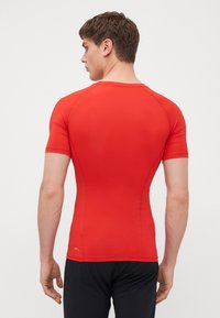 Rød kortermet treningsskjorte, tettsittende design, glatt tekstur, sømløs søm, bakview, kombinert med mørke shorts.