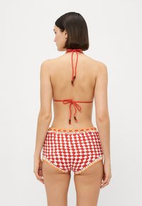 Rode gehaakte bikini-top met halternek en kralenaccenten; bijpassende hoogtaille onderkant met witte diamantpatronen.