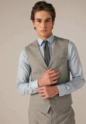 Gilet grigio a quadri sopra una camicia azzurro chiaro con motivo, caratterizzato da un colletto stretto e dettagli nei polsini, con una cravatta abbinata, su uno sfondo neutro.