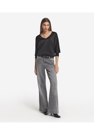 Blouse en satin noir avec un décolleté en V et des manches trois-quarts, associée à un jean large gris et des chaussures à talons noires. Design simple.
