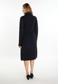 Rochie neagră cu guler �înalt, corp solid și mâneci lungi cu paiete, având fante laterale și o textură netedă. Purtați-o cu pantofi negri.