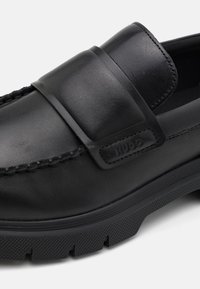 Black leather loafers with a wide strap across the instep, textured rubber sole, and stitching detail along the upper edge. HUGO branding evident.