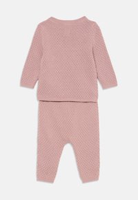 Ensemble en tricot rose constitué d'un pull texturé à manches longues et d'un pantalon assorti. Chaque pièce présente un col et des poignets côtelés.