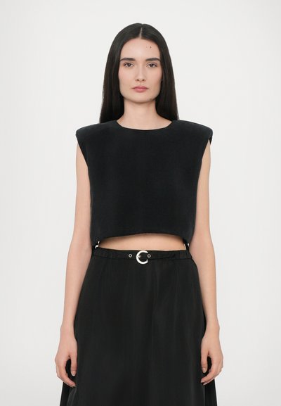Haut noir court avec des épaules structurées, fabriqué à partir d'un matériau doux, accompagné d'une jupe noire avec une boucle de ceinture en argent circulaire.