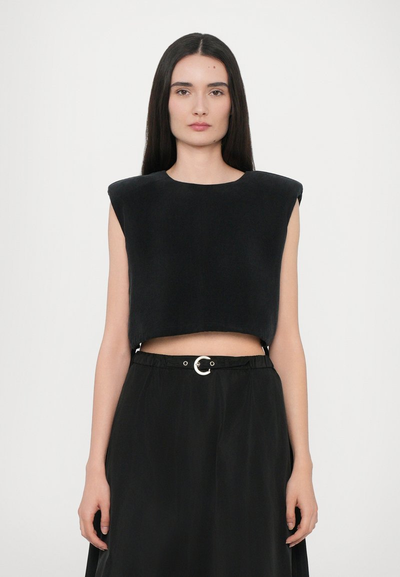 Zwarte cropped top met gestructureerde schouders, gemaakt van een zacht materiaal, gecombineerd met een zwarte rok met een ronde zilveren riemgesp.