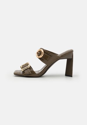 Mule con tacco in similpelle coccodrillo marrone, con due inserti a fibbia color oro e punta quadrata. Design con tacco a blocco e texture liscia.
