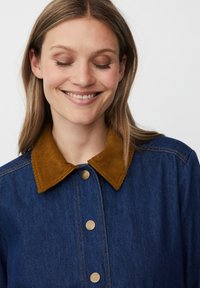 Denimová bunda se zlatými knoflíky a hnědým kordovým límcem. Disponuje modrou tkaninou s viditelným šitím, střední hmotností a volným střihem.