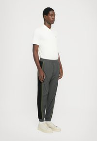 Polo shirt blanc avec un col, pantalon de sport gris avec des rayures latérales vertes, et baskets blanches. Tissu lisse et coupe confortable.